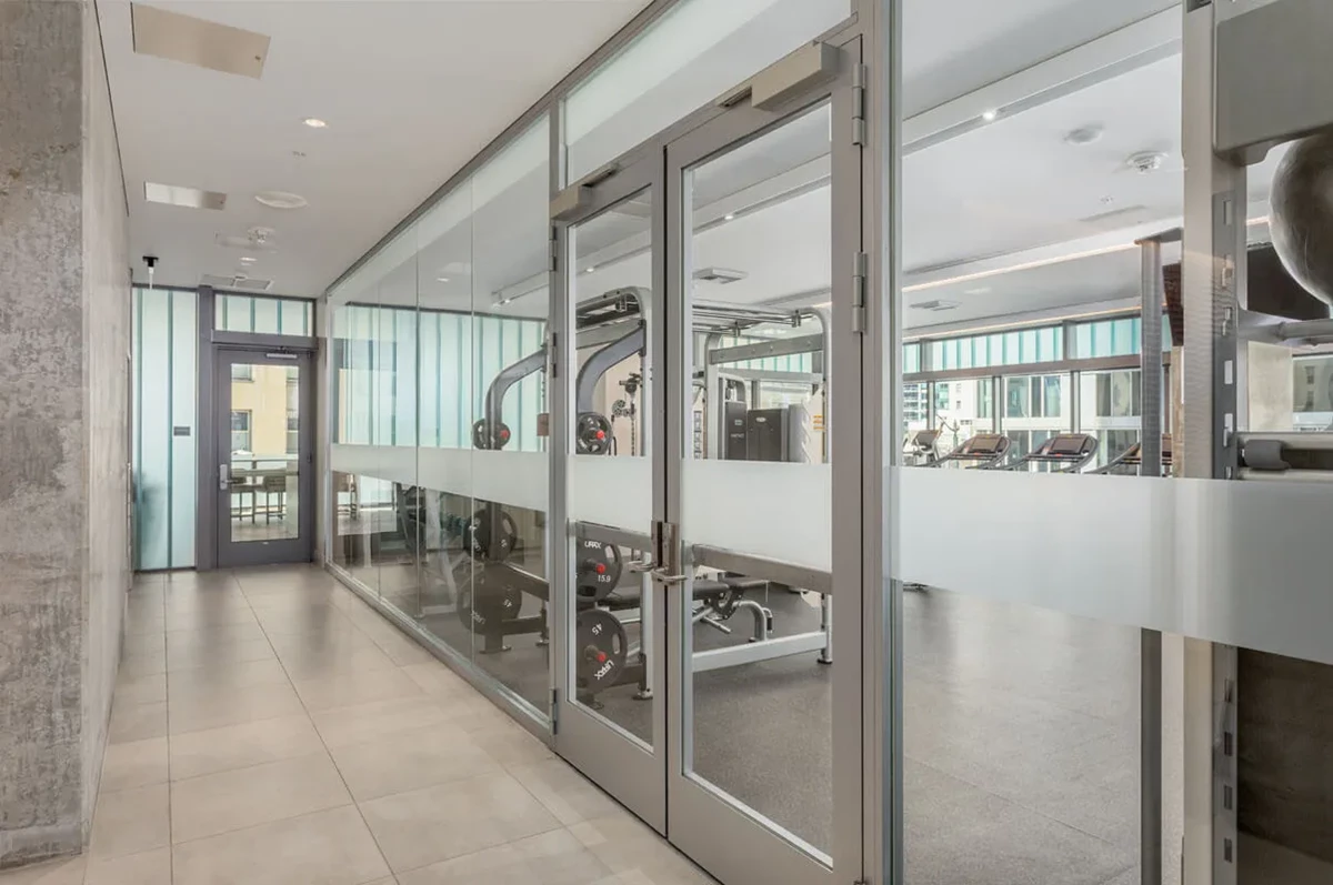 Modern gym with glass walls, showcasing fitness equipment and city view.